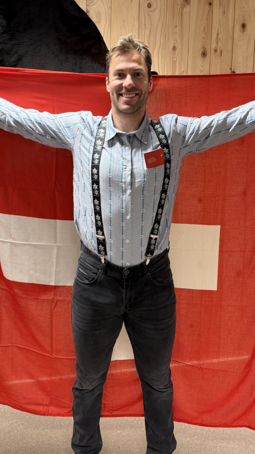 devos posant en chemise typique helvétique et arborant un drapeau suisse